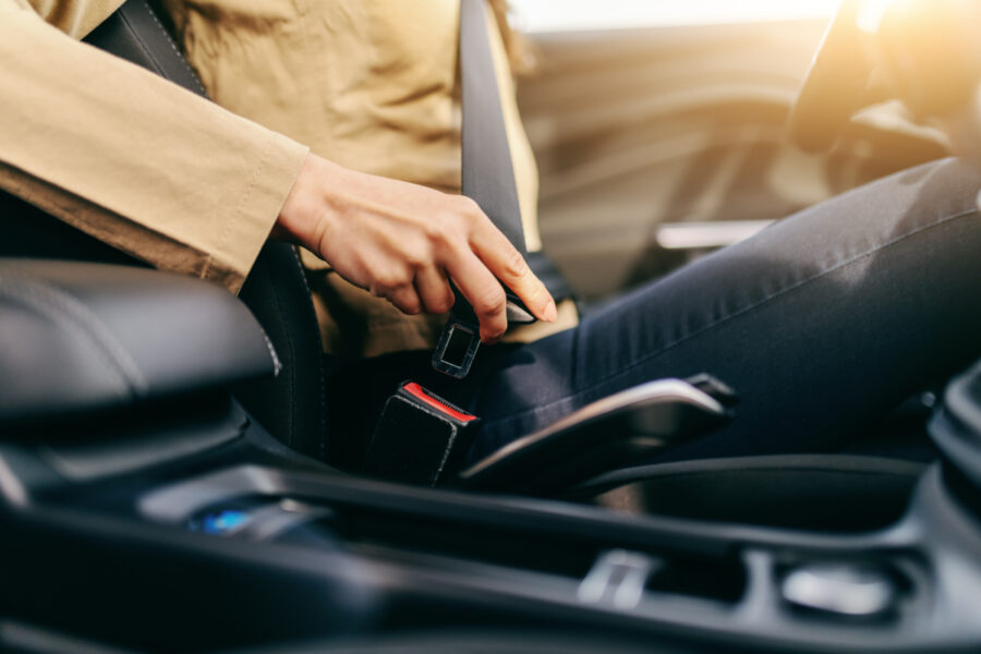 Close up of caucasian woman fastening seat belt in her car. Selective focus on hand.