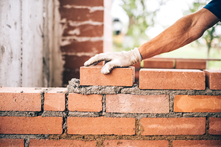 industrial bricklayer worker placing bricks on cement while building exterior walls, industry details