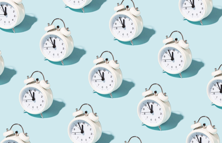 Pattern made of white alarm clocks on blue background. Trendy conceptual photo with open composition.