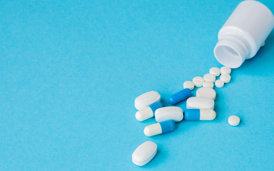 Close up pills spilling out of pill bottle on blue background. Medicine, medical insurance or pharmacy concept.